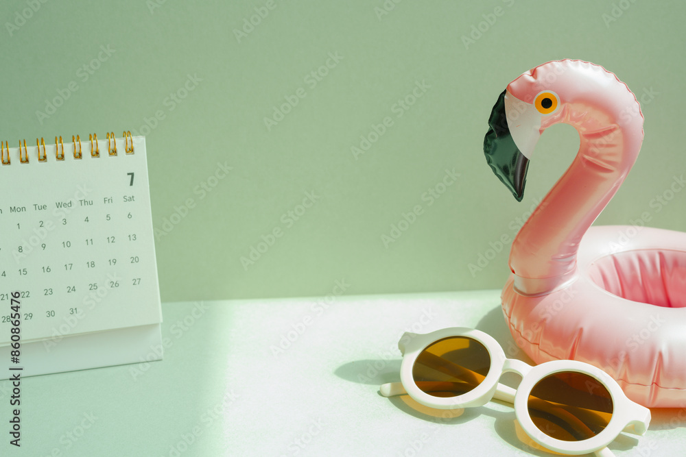 Summer vacation planning concept. Pink flamingo bird shape swimming pool tube and sunglasses, calendar on mint green background