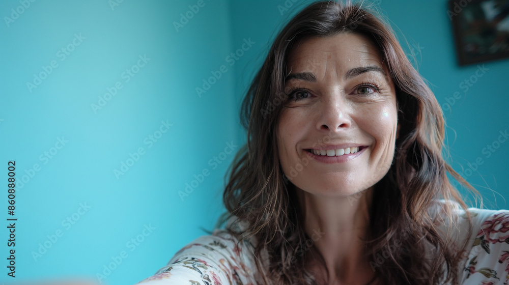 Mother, approximately 45 years old, in a blue room, recording herself as a selfie, smiling at the camera