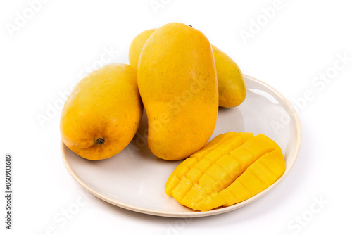 Three yellow Ataulfo mangos on a plate with half a mango cut into cubes isolated on white