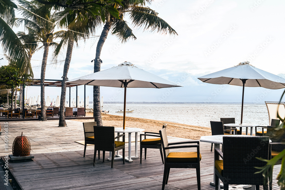Fototapeta premium Cafe and restaurant chairs with table and umbrella at beach. Famous travel destination in Sanur, Bali, Indonesia.