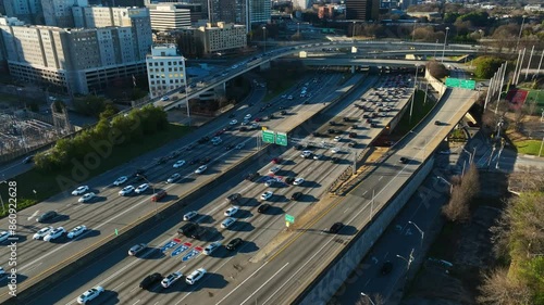 Cars leaving busy interstate highway of american town at sunrise. Downtown buildings and homes with bridge in USA. Atlanta City in Georgia. Aerial top down shot.