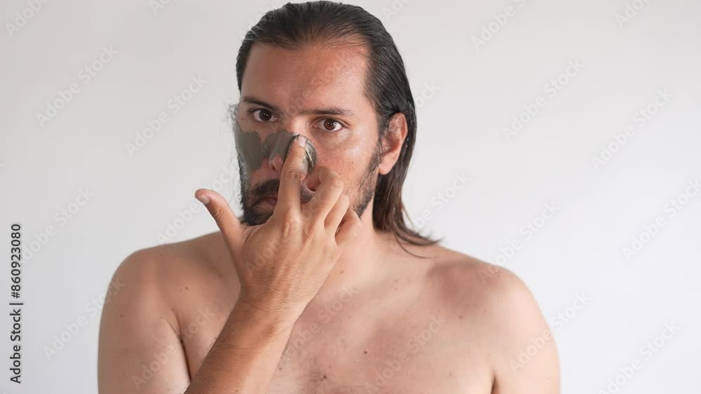 The man takes care of the skin of the face. A man put a clay mask on his face in front of a mirror, clay The man takes care of the skin of the face. A man put a clay mask on his face in front of a mirror, clay