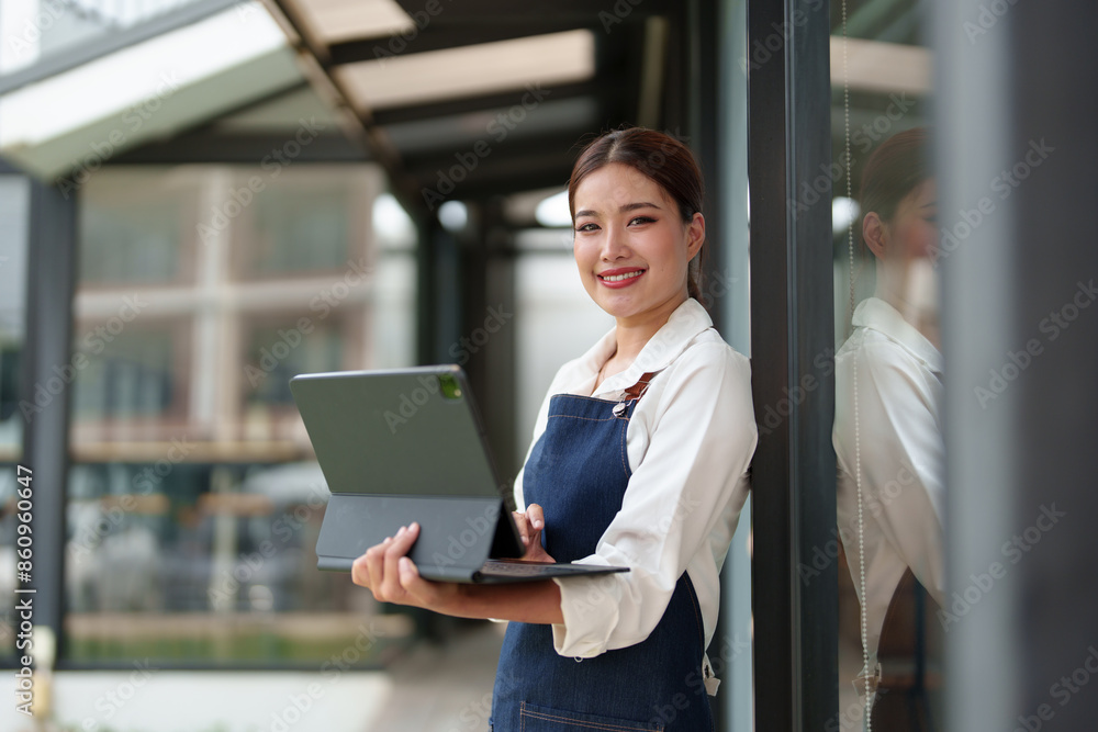 Happy Asian businesswoman is a waitress in an apron. The coffee shop owner stood at the door with a laptop for administrative purposes. Small business ideas, coffee shops and restaurants. Happy Asian businesswoman is a waitress in an apron. The coffee shop owner stood at the door with a laptop for administrative purposes. Small business ideas, coffee shops and restaurants.
