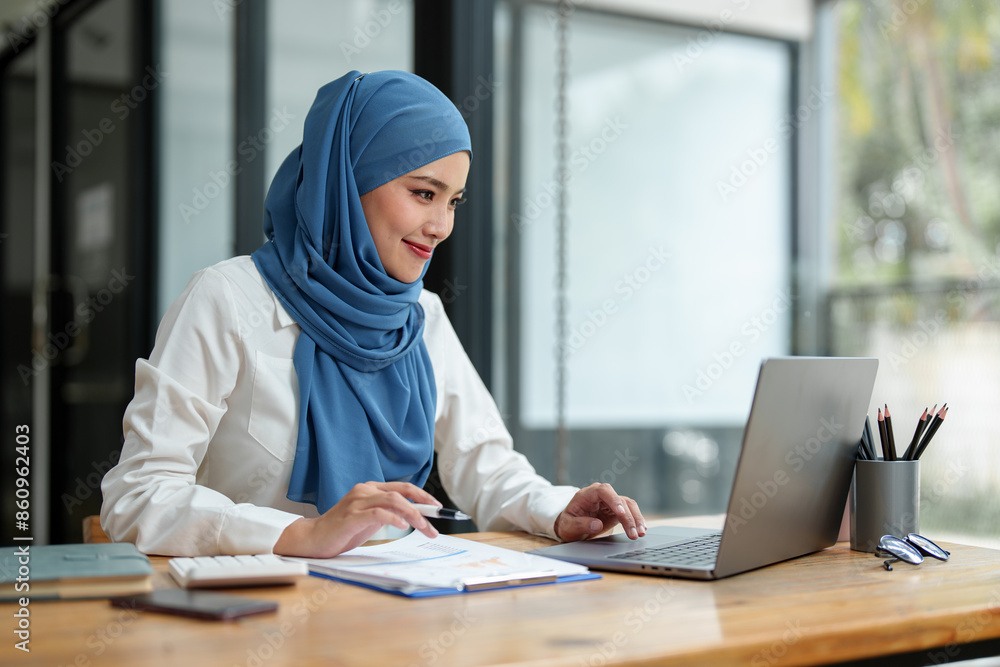 Modern office Muslim businesswoman wearing hijab sits with laptop online, doing paperwork Sitting and working on financial projects, analysis, calculations, startup business ideas, e-commerce, online. Modern office Muslim businesswoman wearing hijab sits with laptop online, doing paperwork Sitting and working on financial projects, analysis, calculations, startup business ideas, e-commerce, online.