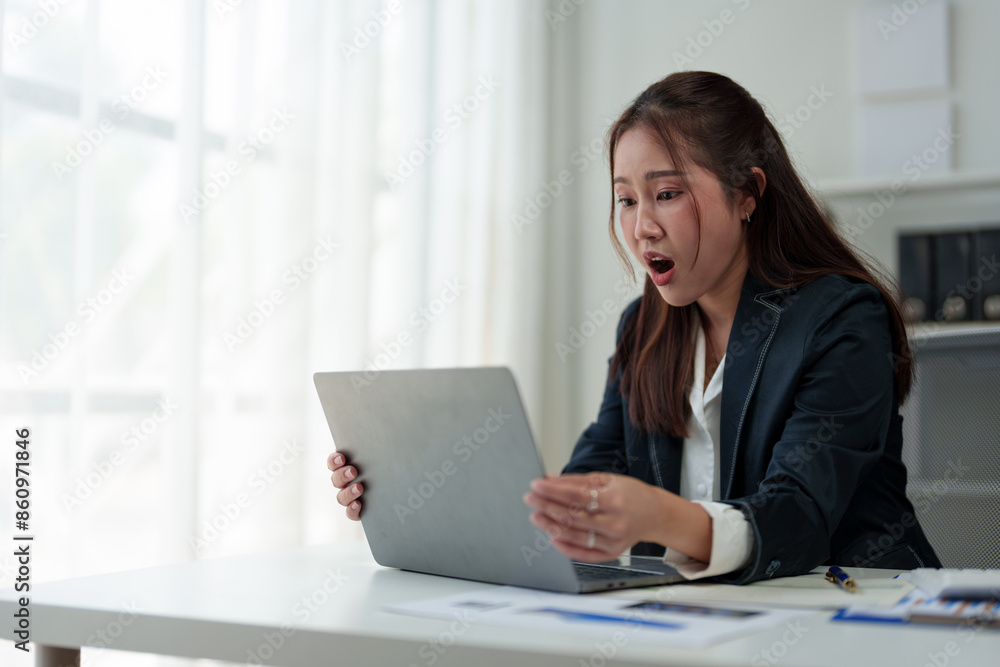 Surprised and happy businesswoman shows joyful expression after viewing news results, business approval results and financial approval results on laptop at office. Startup business growth concept. Surprised and happy businesswoman shows joyful expression after viewing news results, business approval results and financial approval results on laptop at office. Startup business growth concept.