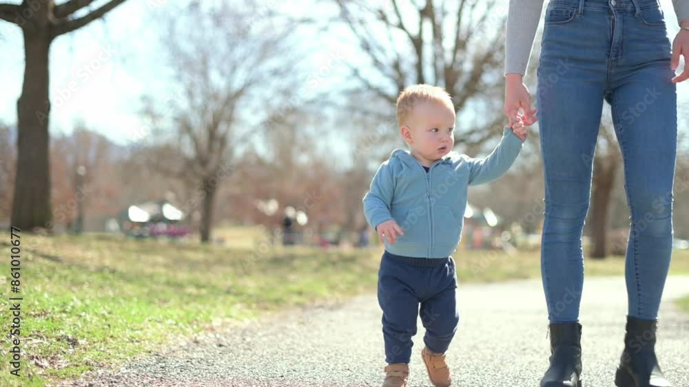 A mother holding hands with her toddler as they walk together in a park on a sunny day, enjoying a moment of exploration and bonding. High quality 4k footage A mother holding hands with her toddler as they walk together in a park on a sunny day, enjoying a moment of exploration and bonding. High quality 4k footage