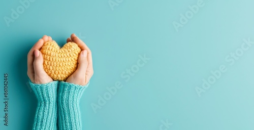Hands in cozy sweaters holding a knitted heart shape against a turquoise background, symbolizing love, care, and warmth.
