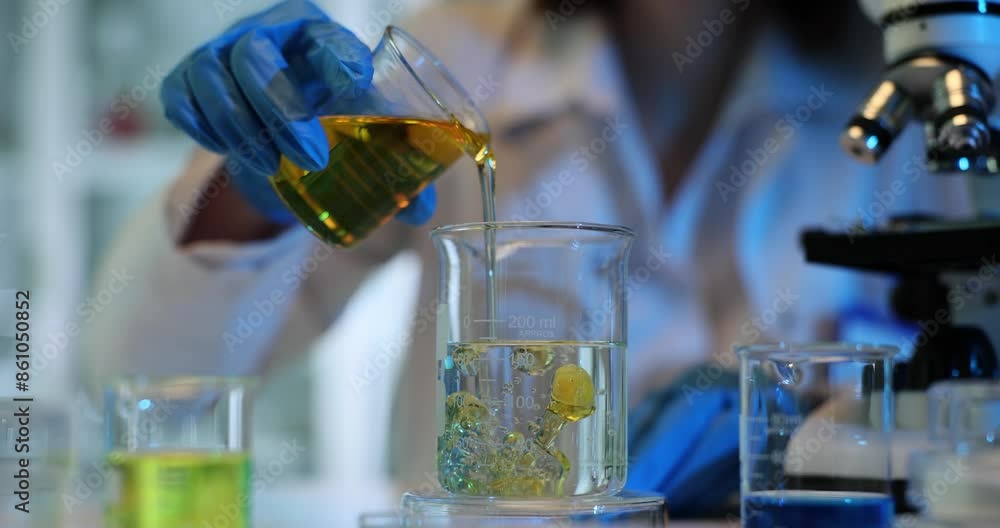 Technician pours plant oil into beaker of water in lab Technician pours plant oil into beaker of water in lab