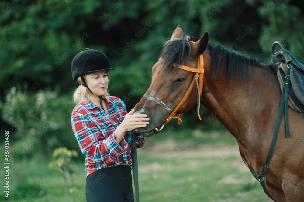 Obraz premium Happy blonde with horse in forest. Woman and a horse walking through the field during the day. Dressed in a plaid shirt and black leggings.