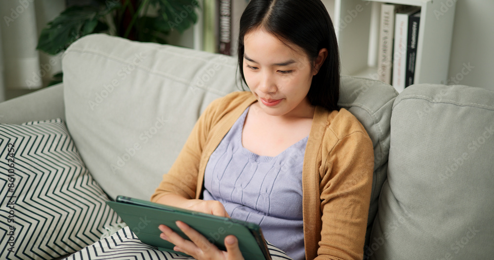 High angle view, Young asian woman sitting relaxing on the sofa playing social media on digital tablet in the living room at morning ,spend free time High angle view, Young asian woman sitting relaxing on the sofa playing social media on digital tablet in the living room at morning ,spend free time