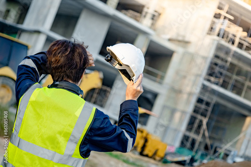Dizziness and migraine headache from overworked exhaustion or heat stroke. Tired Asian male worker taking off safety helmet touching forehead while working at construction site in extremely hot day