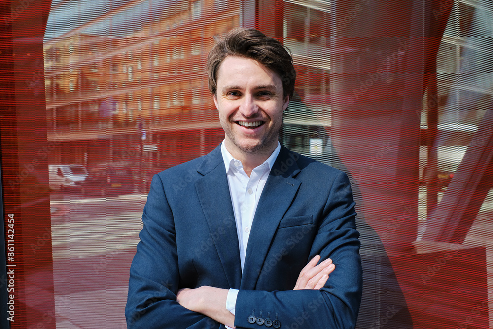Smiling businessman standing with arms crossed and leaning on red glass Smiling businessman standing with arms crossed and leaning on red glass