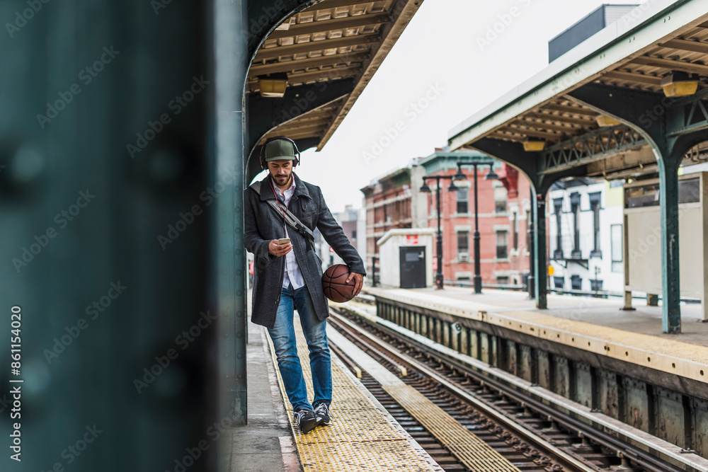 Young man using phone with basketball leaning on column waiting at station Young man using phone with basketball leaning on column waiting at station