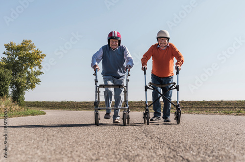 Senior friends wearing safety helmets competing for wheeled walker race photo