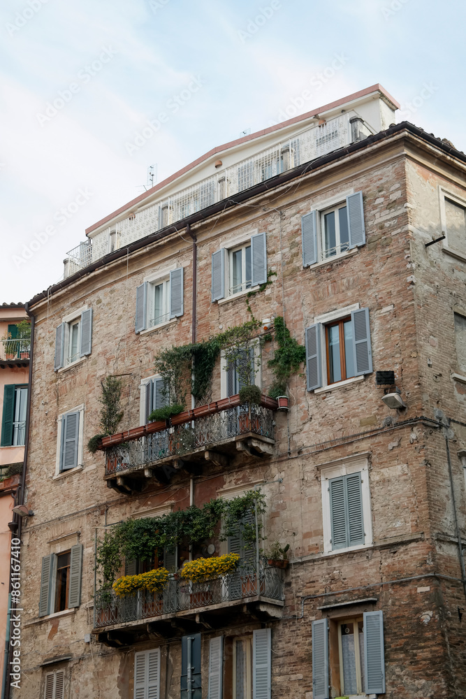 Beautiful old brick building facade with balconies, greenery and shutters on the windows in Perugia (Italy). Beautiful old brick building facade with balconies, greenery and shutters on the windows in Perugia (Italy).