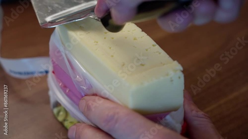 White Jarlsberg cheese sliced slowly with cheese slicer, close up photo