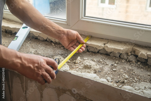 Worker measuring old window sill before renovation at home.