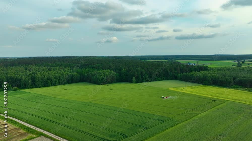 Aerial view of green fields with a tractor working near a forest under a partly cloudy sky. Aerial view of green fields with a tractor working near a forest under a partly cloudy sky.