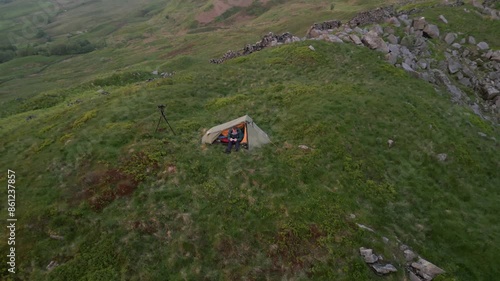 A solo traveller made his tent on a green rocky hill at sunset towards Errwood Reserve, UK photo