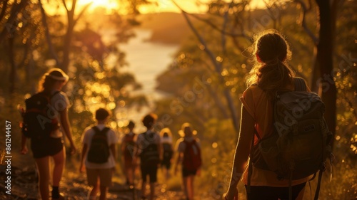 A group of friends hiking through a forest with a stunning sunset over a rocky shoreline in the background. AIG53M photo