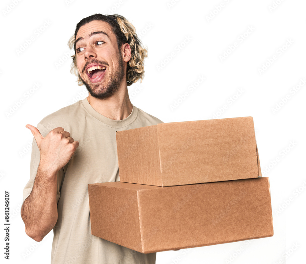 Young man with cardboard boxes in studio points with thumb finger away, laughing and carefree. Young man with cardboard boxes in studio points with thumb finger away, laughing and carefree.