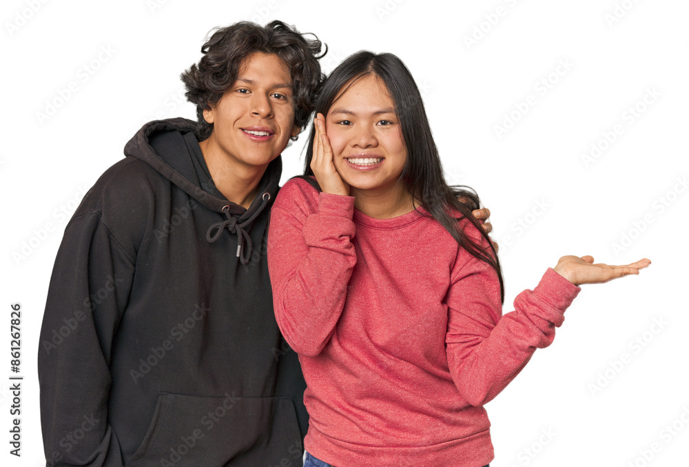 Young interracial couple in studio holds copy space on a palm, keep hand over cheek. Amazed and delighted. Young interracial couple in studio holds copy space on a palm, keep hand over cheek. Amazed and delighted.