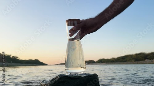 Hand placing a caraf with fresh water on a rock in middle of a river, during sunset photo