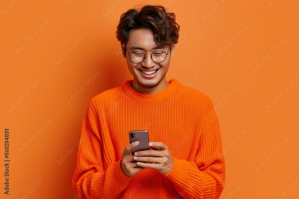 A man in an orange sweater using a smartphone against an orange background A man in an orange sweater using a smartphone against an orange background