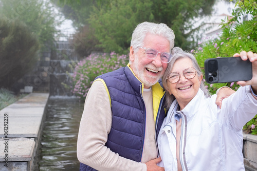 Happy senior couple outdoor in the park get a selfie by mobile phone, grey haired husband and wife enjoying tender moment, happy marriage, sincere feelings © luciano