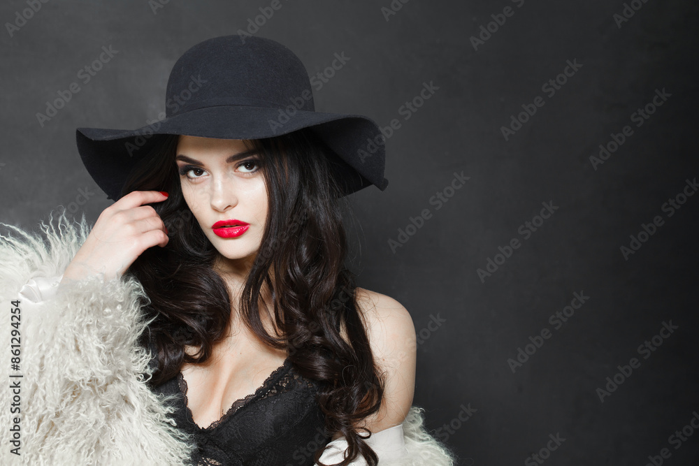 Sensuality young adult woman fashion model with bright make-up and long wavy hair wearing blue hat posing against blue studio wall background Sensuality young adult woman fashion model with bright make-up and long wavy hair wearing blue hat posing against blue studio wall background