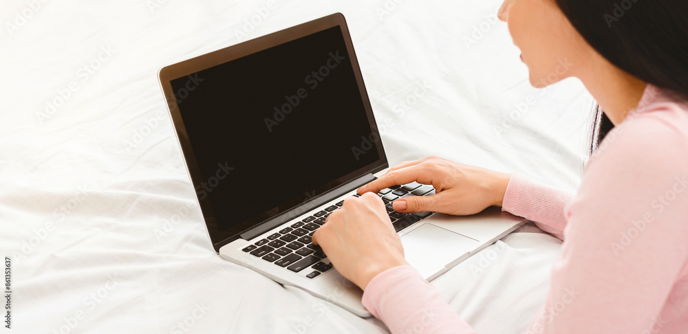 A woman is seated on a bed, attentively using a laptop computer with blank screen in front of her. She appears focused on her screen, typing and clicking, cropped A woman is seated on a bed, attentively using a laptop computer with blank screen in front of her. She appears focused on her screen, typing and clicking, cropped