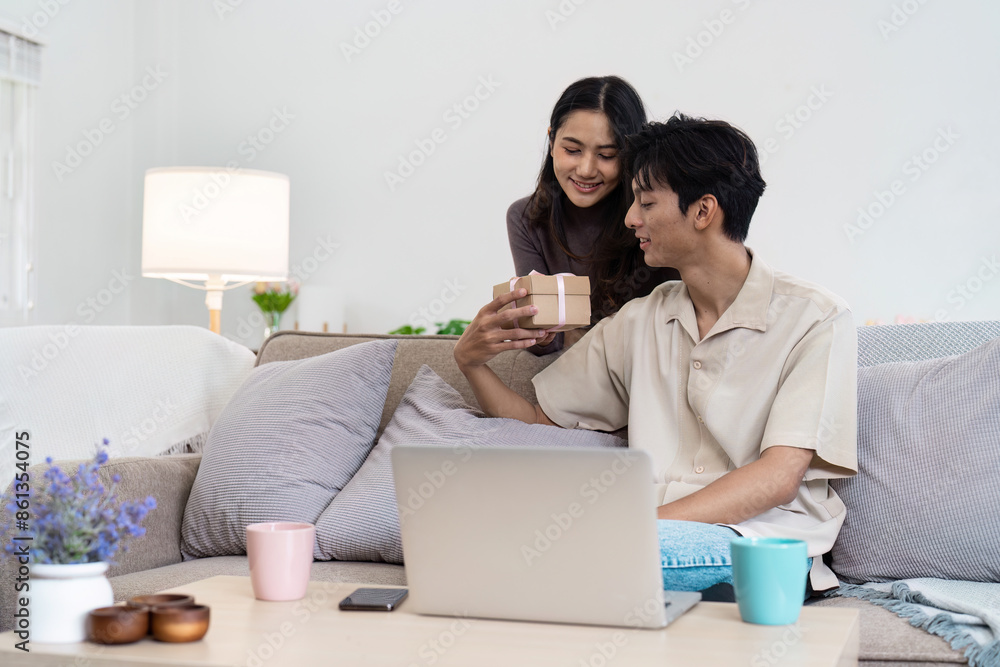 Young Couple Enjoying Quality Time Together at Home, Exchanging Gifts and Relaxing in a Cozy Living Room Setting Young Couple Enjoying Quality Time Together at Home, Exchanging Gifts and Relaxing in a Cozy Living Room Setting