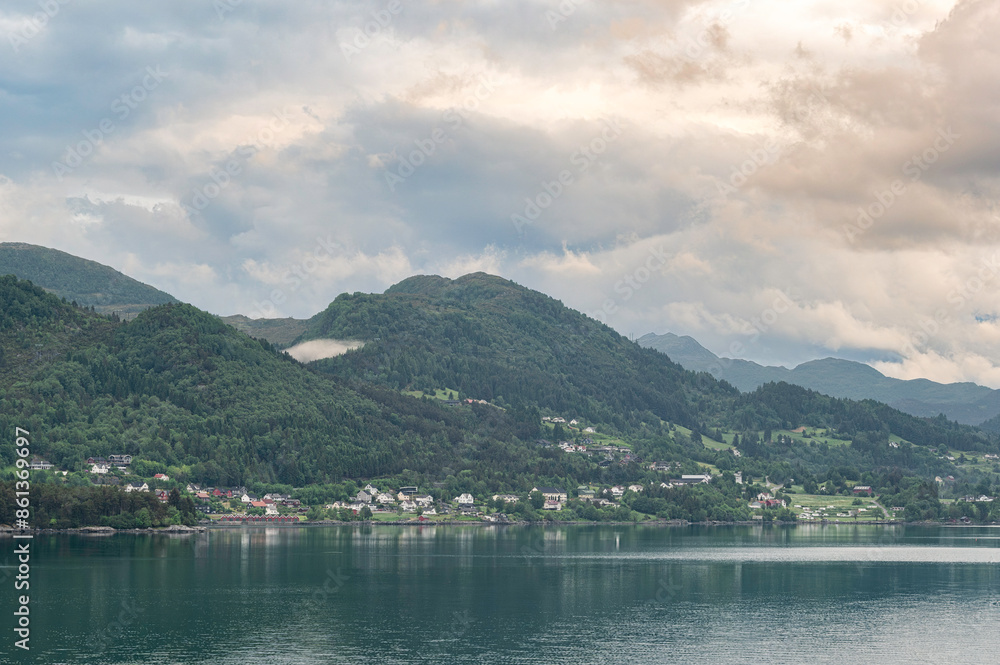 Norwegian village landscape with fjord, mountains, clouds and colorful houses. Location is Nordfjord, near Olden, Norway Norwegian village landscape with fjord, mountains, clouds and colorful houses. Location is Nordfjord, near Olden, Norway