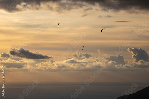 Paragliders gliding in the backlight in Ölüdeniz with the light filtering through the clouds