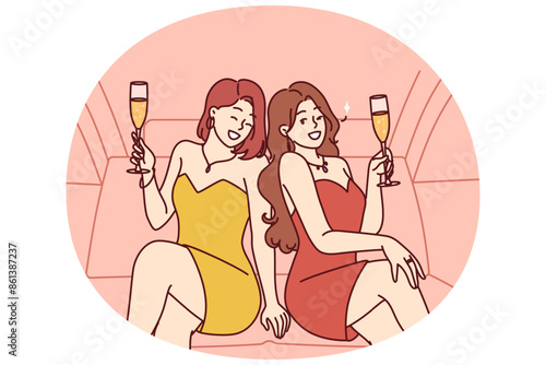 Celebrity women sit in luxury car with glasses filled with sparkling wine during pre-wedding bachelorette party. Celebrity girls in evening dresses riding in limousine enjoy premium atmosphere