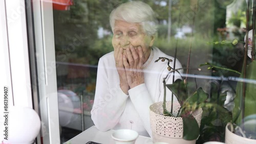 Lonely elderly woman looking out the window, waiting for someone to visit her