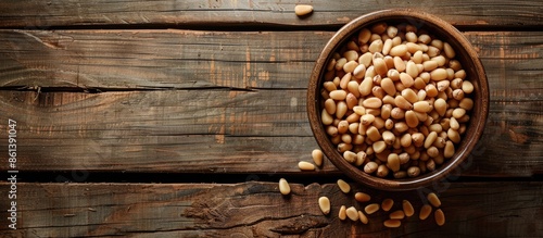 Top view of a bowl with pine nuts on a wooden background, providing space for a text overlay or other elements in the image. copy space available