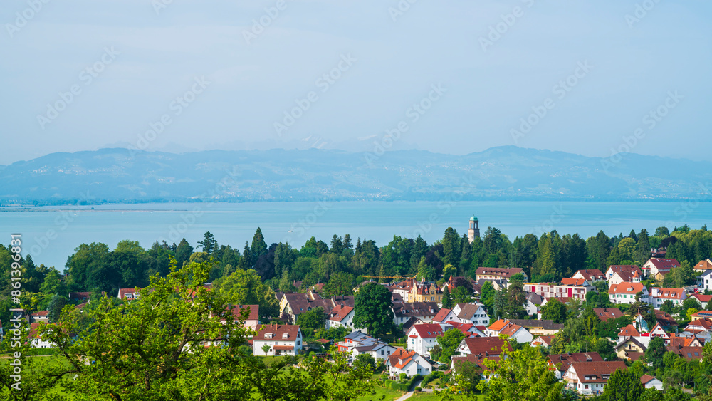 Germany, Bad schachen tower, houses, buildings, and green trees surrounded by silent bodensee lake water early in the morning after sunrise, aerial panorama landscape view to swiss mountains