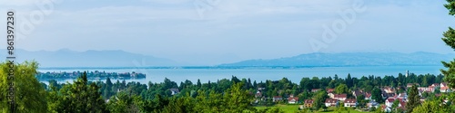 Obraz na płótnie Germany, Lindau, XXL aerial panorama view above lindau island, bad schachen tower, lighthouse, city, tree tops and silent lake water early morning after sunrise, foggy view to swiss alps w salonie