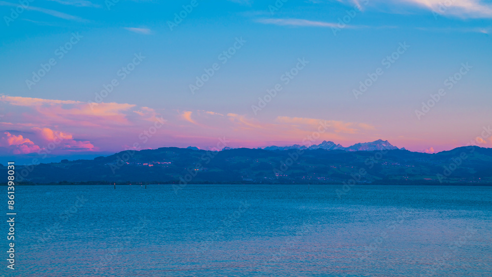 Germany, Warm sunset light on alps mountains nature landscape behind water of bodensee lake after sunset, panorama view from lindau to swiss coastline and saentis mountain