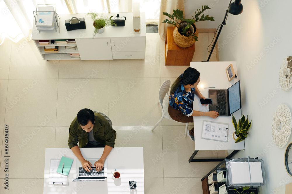 © DragonImages - Top view of young colleagues sitting at their workplaces and working on computers in modern office © DragonImages - Top view of young colleagues sitting at their workplaces and working on computers in modern office