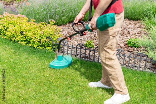 Tableau sur toile Man cutting fresh green grass with an electric trimmer on his garden lawn, takin