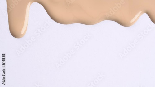 Foundation cream for face, BB cream, CC cream or concealer pouring on white background, macro shot. Cosmetic liquid foundation, or cream beige color smudge flowing down on a white surface.