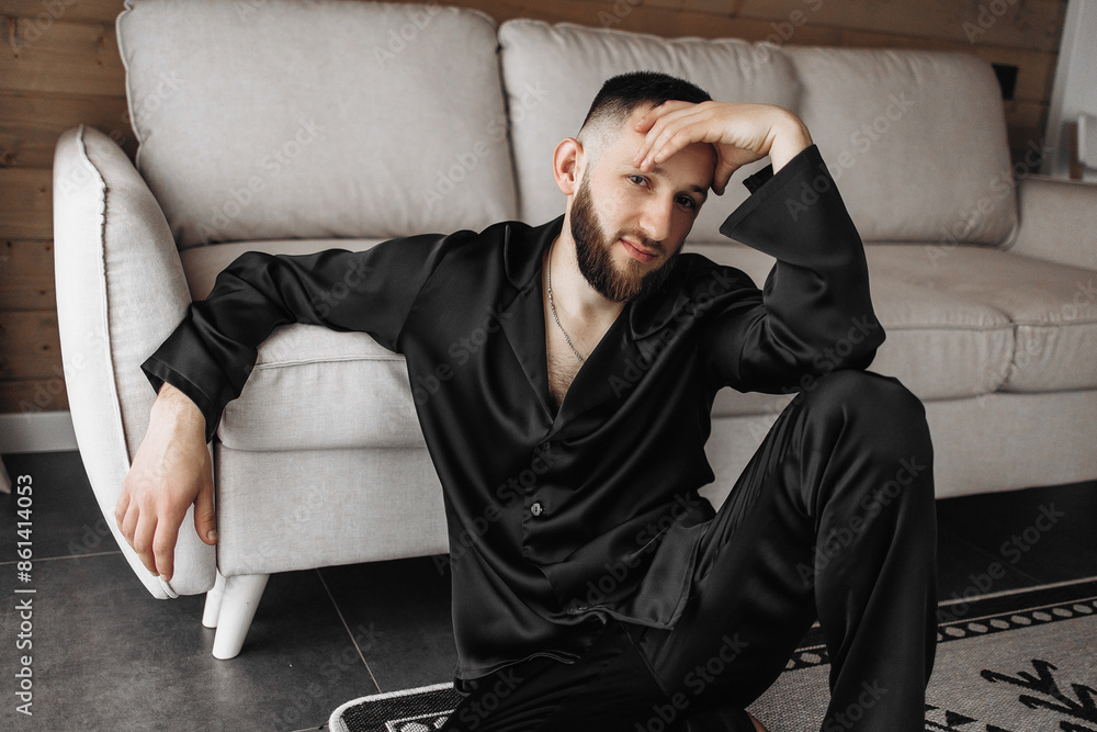 A man in a black shirt and pants is sitting on a rug in a living room. He is looking at the camera with a smile on his face A man in a black shirt and pants is sitting on a rug in a living room. He is looking at the camera with a smile on his face
