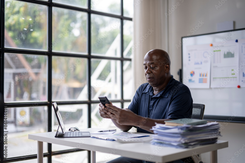 A man is sitting at a desk with a laptop and a cell phone A man is sitting at a desk with a laptop and a cell phone