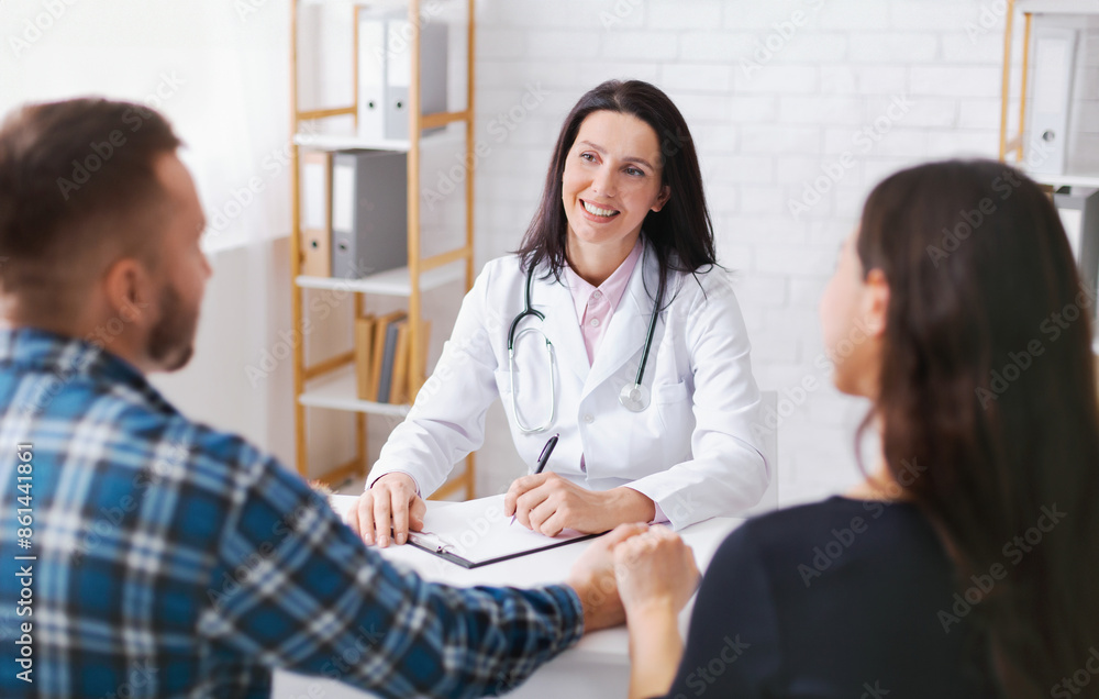Woman doctor in a white coat sits at a table with a couple, taking notes. She is smiling and appears to be listening attentively to the couple. T Woman doctor in a white coat sits at a table with a couple, taking notes. She is smiling and appears to be listening attentively to the couple. T