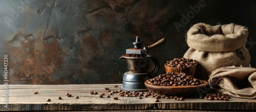 An old wooden table displayed roasted coffee beans in sacks, crushed coffee, and a hand cranked grinder all ready to be served on a spoon against a copy space image.