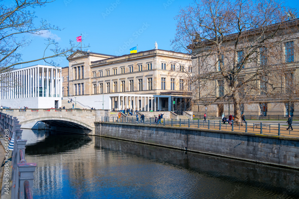 Naklejka premium Clear skies over the New Museum with visitors walking along the riverbank in Berlin, Germany.