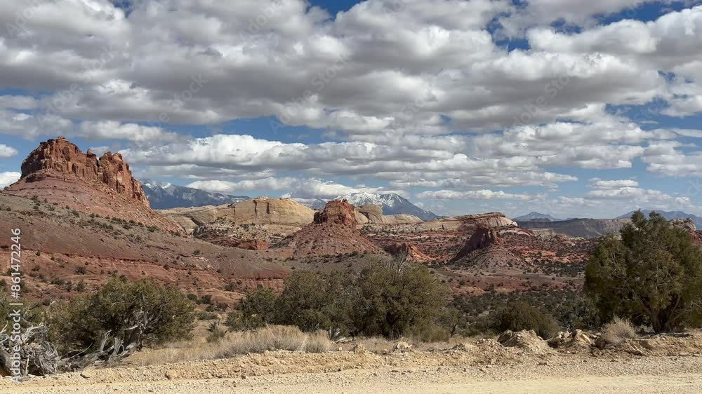View of the Waterpocket Fold in Capitol Reef National Park, Utah. Red rock formations with snow-capped mountains in the distance under a blue sky with clouds. Shot from the Burr Trail Road - USA View of the Waterpocket Fold in Capitol Reef National Park, Utah. Red rock formations with snow-capped mountains in the distance under a blue sky with clouds. Shot from the Burr Trail Road - USA