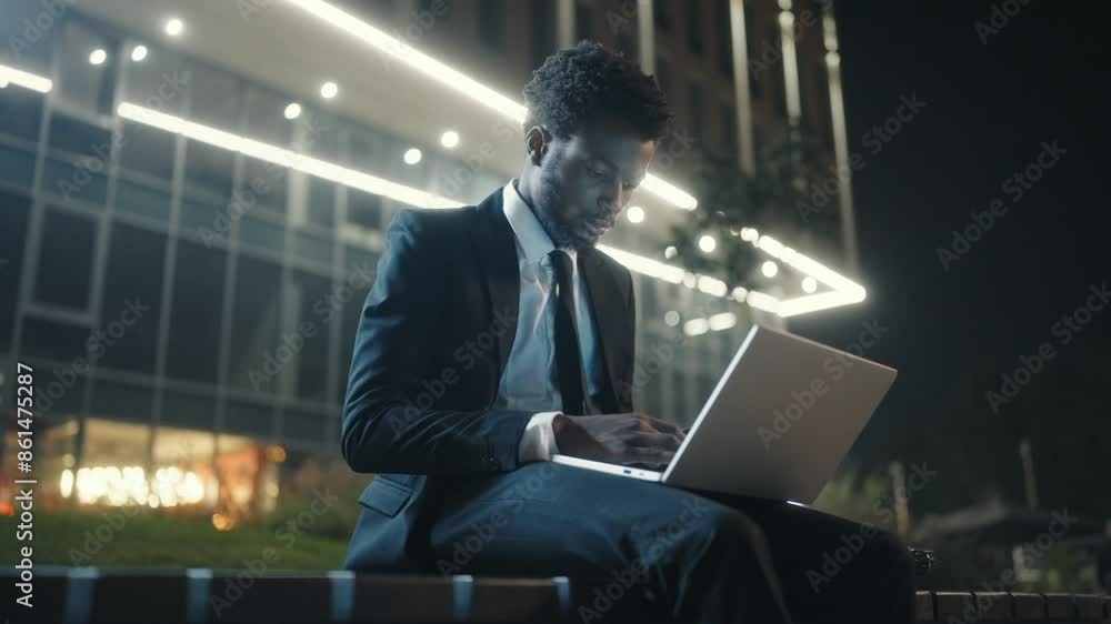 African American man sitting at bench and working with laptop. Concentrated man wearing business suit. Male using laptop outside. Male director sitting outdoor at business center. Ethnic diversity. African American man sitting at bench and working with laptop. Concentrated man wearing business suit. Male using laptop outside. Male director sitting outdoor at business center. Ethnic diversity.